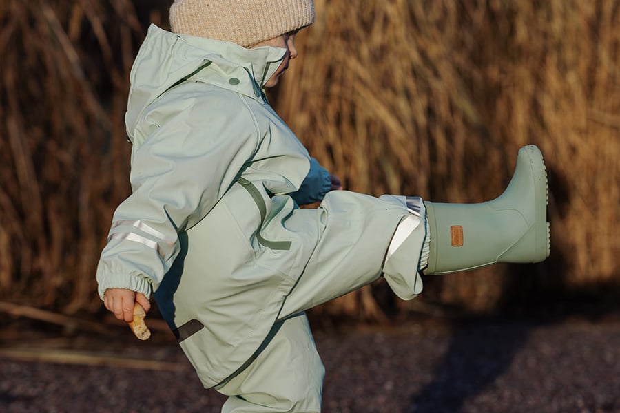 Ett barn iklädd regnkläder som sträcker upp ena benet, har på sig gummistövlar.