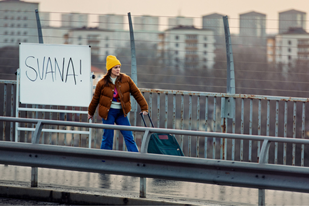 Kvinna drar en tavla som står Svana på en bro