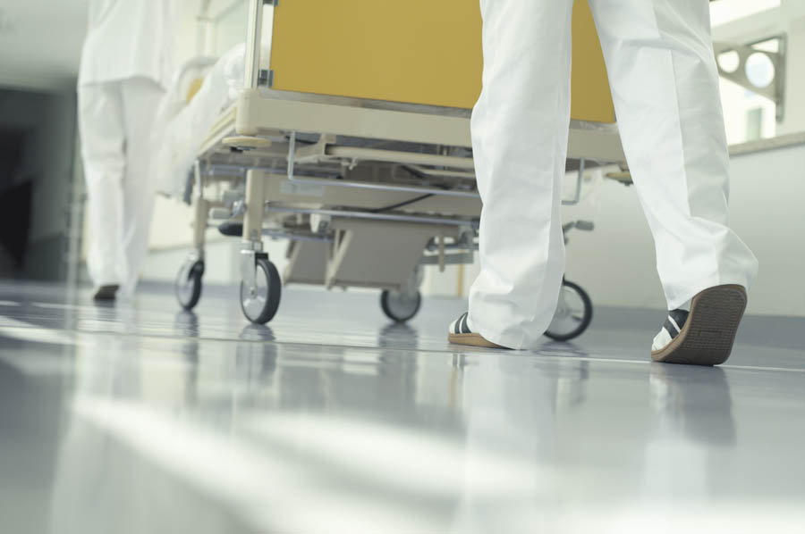 Ett par ben klädda i sjukhuskläder som rullar en säng framför sig